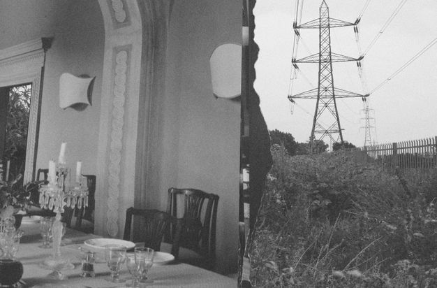 Black and white images. To our left, we look across a dining table set with plates and glasses at the wall of the room. To our right, power lines march back from a meadow of grasses and flowers.